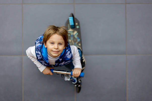Cute child, school boy in a shopping mall, using escalator, riding push scooter