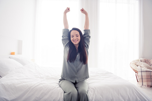 Photo portrait of lovely young lady stretch arms prepare bedtime wear trendy gray sleepwear isolated on white bedroom indoor interior.