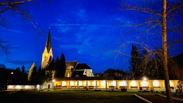 Oberstdorf, Germany - March, 14th - 2024:Public park, illuminated benches and the Catholic Church in the background.