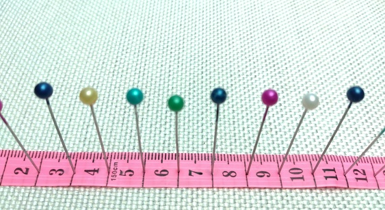 sewing needles and pins of different colors, ruler on white cloth background