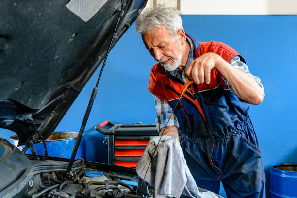 a senior mechanic man is checking the oil in a car. - old men car oil imagens e fotografias de stock