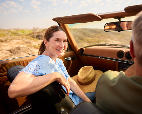 Retired Senior Couple On Vacation Driving In Classic Sports Car On Road Trip Through Countryside