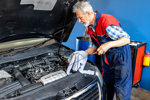 An Older Professional Car Mechanic Checking the Condition of the Car and Level of Motor Oil.