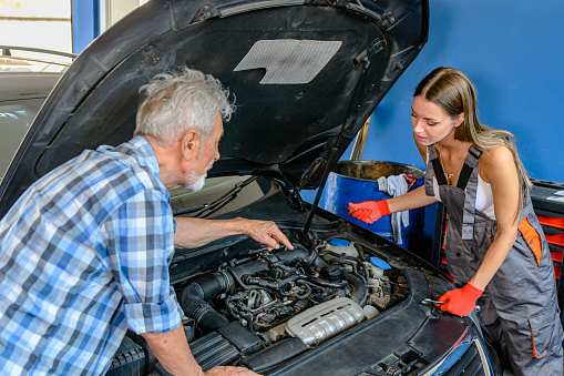 Senior Auto Mechanic is Teaching his Younger Female Assistants about Fixing the Problems with the Car.