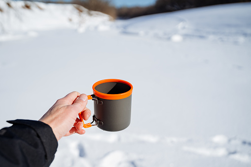 The person is holding a cup of hot liquid in Drinkware while standing in the freezing snowcovered landscape, as Eyewear protects from the bright sun glare on the white snow and asphalt