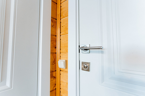 A detailed shot of a white home door with a wooden fixture and a door handle. The hardwood door contrasts beautifully with the woodstained wall behind it