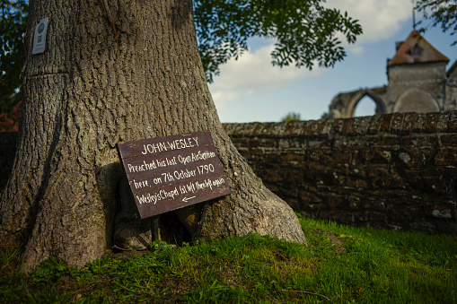 Winchelsea, East Sussex - A hand painted wooden sign noting the last open air sermon by Methodist, John Wesley and providing directions to Wesley's Chapel. Shallow depth of field with a part of The Church of St Thomas the Martyr and a wall in the background.