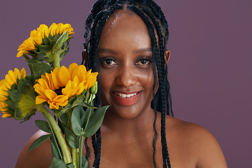 Portrait of cheerful Black young woman with braided hair holding sunflowers