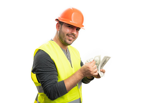 Constructor man wearing orange safety helmet and fluorescent vest making cheerful happy expression counting cash money with blank copyspace isolated on white
