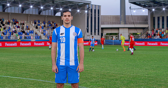 Portrait of male football player in blue jersey standing on pitch during match.