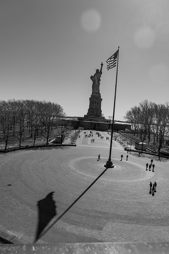 Liberty Island, New York, USA - March, 2024.  Statue of Liberty on Liberty island with tourists in the foreground near the flag pole in front of the Statue of Liberty museum.
