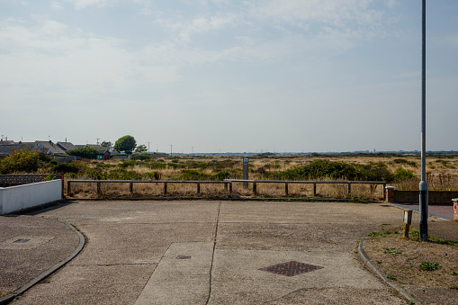 The end of a concrete road overlooking scrubland and houses on a sunny day.