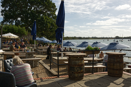 People enjoying food and drink on the waterfront terrace of the Crown and Anchor pub at Dell Quay in Chichester Harbour, West Sussex, England