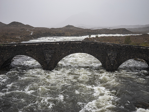 Old stone bridge and rough river during storm in Skye Scotland