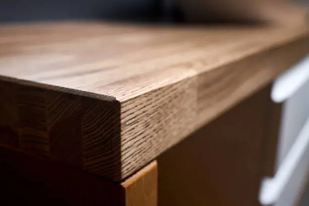 Solid ash glued timber under varnish edge corner table top selective focus macro closeup. Bathroom interior contemporary design countertop tabletop with sink, 16x9.