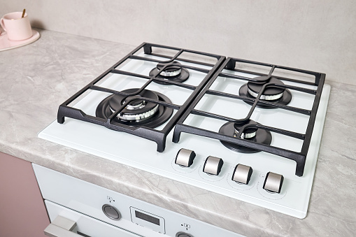 Modern hob gas stove made of tempered white glass using natural gas or propane for cooking products, on light countertop in kitchen interior.