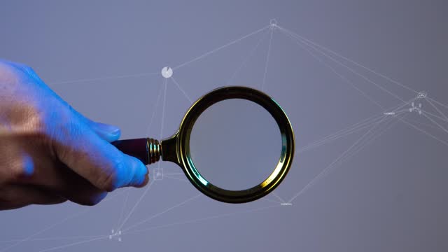 A hand holds a magnifying glass against the background of a moving polygonal network with symbols of the digitalization of human life. Cg