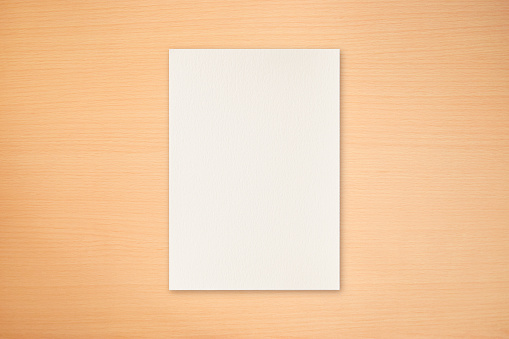 Background of a blank sheet of paper placed on a light wood texture, ideal for use in design work and presentations.