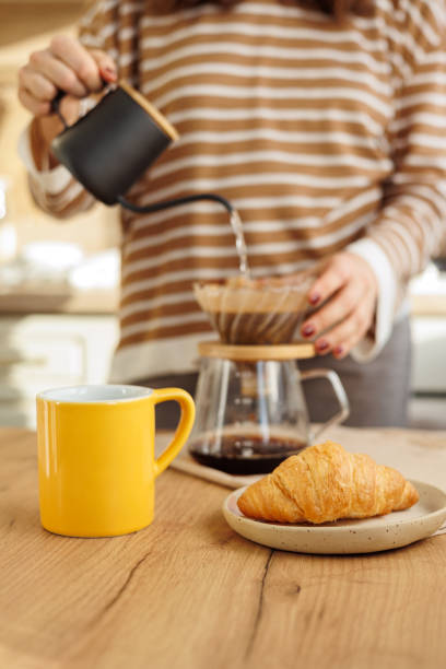 istock female makes coffee in morning kitchen. brews in purover. yellow cup with black coffee drip 2101748430
