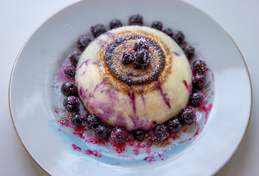 A scrumptious pudding topped with a generous amount of blueberries and sauce on a clean white plate, ready to be enjoyed