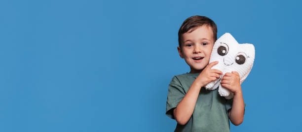 istock A smiling boy with healthy teeth holds a toothbrush and a plush tooth on a blue background. Pediatric dentistry. A place for your text. Panoramic photo. 2101824719