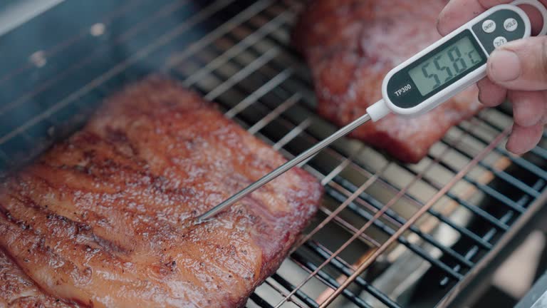 Male hand using meat thermometer checking meat, bacon in smoker oven