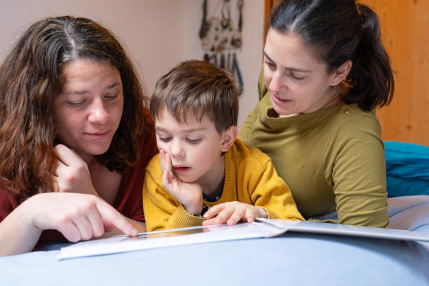 Couple of lesbian mothers watching a book with their son in the bedroom at home Couple of lesbian mothers watching a book with their son in the bedroom at home real wife stories stock pictures, royalty-free photos & images