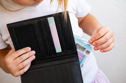child holds black wallet in hand, kid, girl secretly takes money out of parents' wallet, pulls out euro banknotes, concept of pocket money, Personal Boundaries and Trust, Teaching Financial Literacy