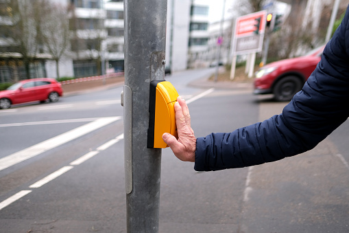 close-up of male hand pushes yellow button on crosswalk, man is going to safely cross road on green light of the traffic light, pedestrian and driver traffic safety concept, observes traffic rules