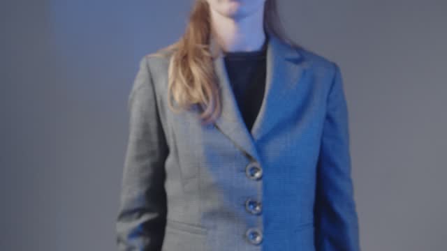 An adult woman in a gray business suit stands and extends her hand with a light pencil. Touch gesture