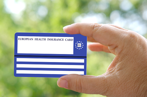 European health insurance card in hand on natural green background, blue EU document healthcare support, medical expenses, emergency, Travel insurance EU and EFTA traveling, healthcare information