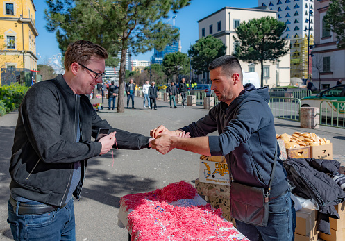 Tirana, Albania. 14 March 2024. Market trader puts on a wristband to a customer, traditionally worn to celebrate Summer Day in Albania.