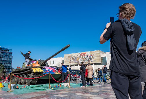 Tirana, Albania. 14 March 2024. A bystander photographs an old tank being spray painted with flowers in Albania by young artists.