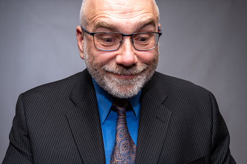 Mature business man facing camera and looking down while smiling on a grey background