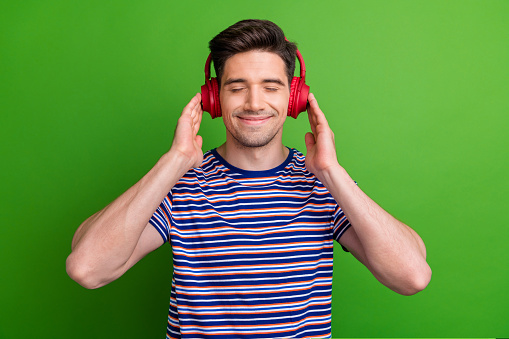 Photo of peaceful carefree person closed eyes arms touch headphones listen favorite music isolated on green color background.