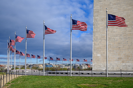 The lower part of the Washington Monument in Washington, DC surrounded by American flags whipping in the wind