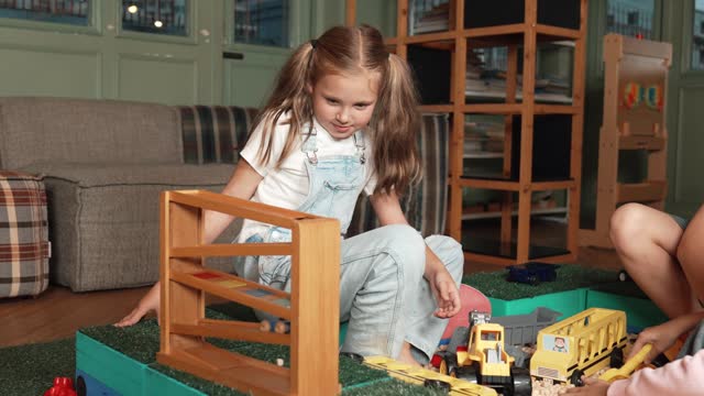 Caucasian girl sits at sand box while placed car model at slope toy. Erudition.