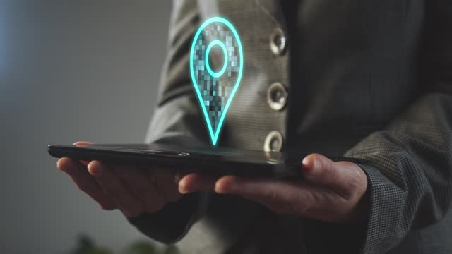 Silhouette of a business woman holding a graphics tablet above the screen of which is a hologram of a location symbol on a map. Cg footage