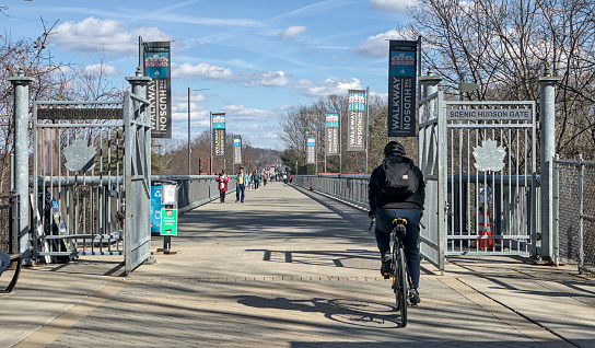 Poughkeepsie, NY - March 16, 2024: Cyclist riding and pedestrians walking across the Walkway Over the Hudson bike path, part of the Empire State Trail in upstate New York.