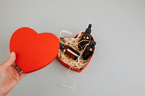 A gift in a cardboard eco package with cosmetics inside on a gray concrete background. Gift box in the shape of heart for Valentine's day in women's hands. Flat lay