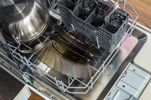 A dishwasher is full of clean dishes, including a large bowl and a few plates. The dishwasher is in the process of being cleaned