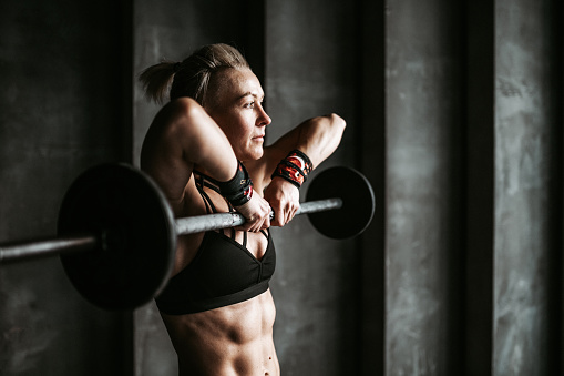 A woman lifting weights in front of a grey wall. Confident woman sport training work out