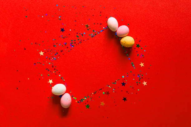 Happy easter decor concept. Festive bright red background with glitter and sparkles, chocolates in the form of Easter eggs. Copy space, flat lay, top view. Blank greeting card, invitation mockup