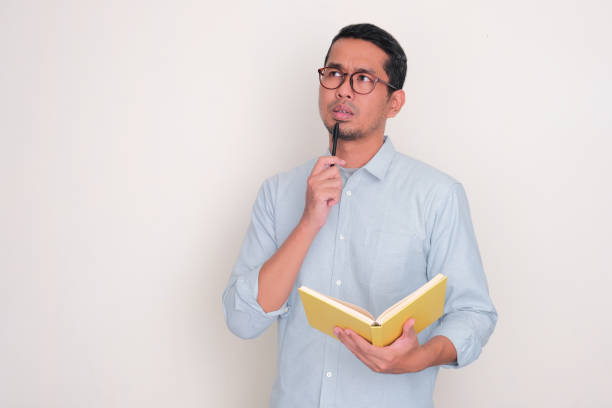 istock Adult Asian man thinking about something while holding a book and pen 2102035629