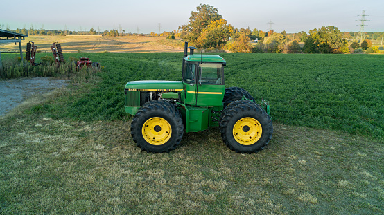 John Deere Green Tractor outside of a barn and farm field taken from a drone at sunset in the fall