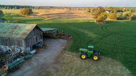 John Deere Green Tractor outside of a barn and farm field taken from a drone at sunset in the fall