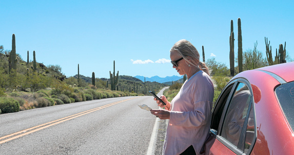 Mature woman looks at map in desert beside vehicle