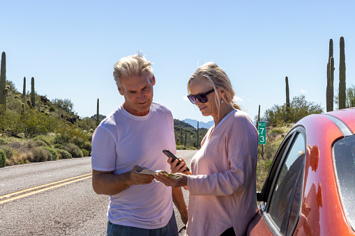 Mature couple park car in desert and look at map for direction on phone and map