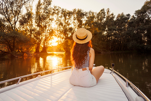 Back view of young woman relaxing while on summer vacation sailing to the sunset on a boat