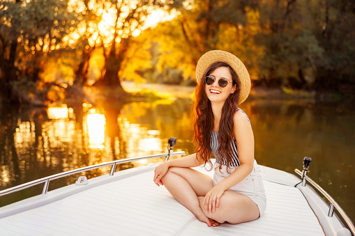 Beautiful young woman relaxing while on summer vacation sailing to the sunset on a boat